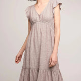 Woman wearing a light brown dress with ruffled sleeves against a plain background